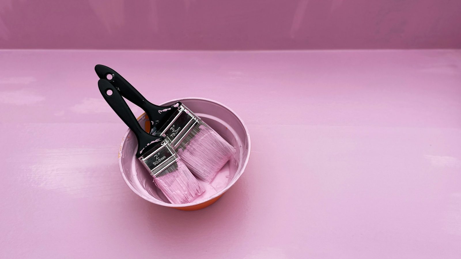 Hair color bowl with two tint brushes on a pink surface