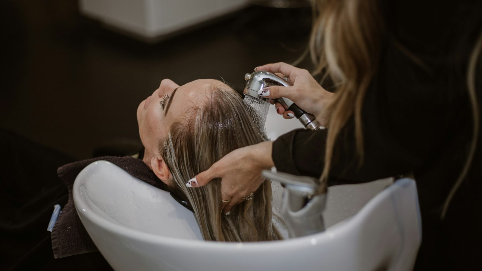 Stylist rinsing a client's hair at a salon shampoo bowl